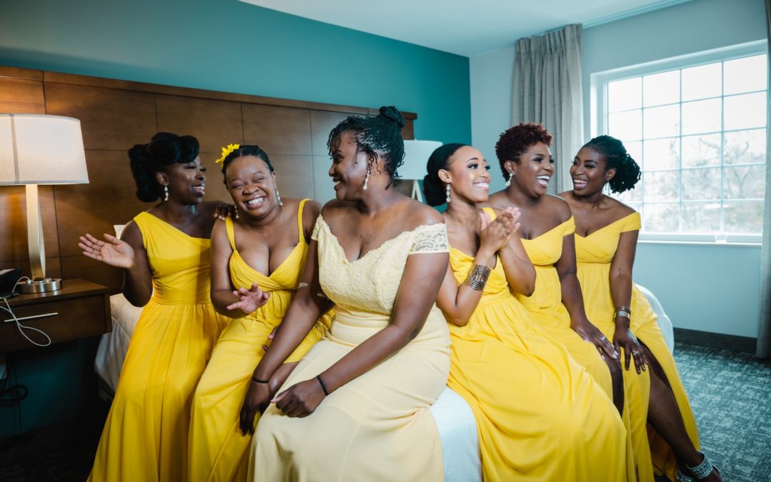 what to pack for your wedding day, picture of bride and bridesmaids sitting on a bed in yellow dresses with the celebrant angel