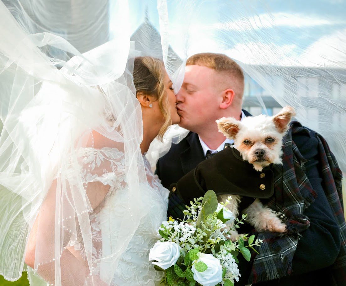 A couple kissing after their ceremony at Meldrum House and their dog in their arms